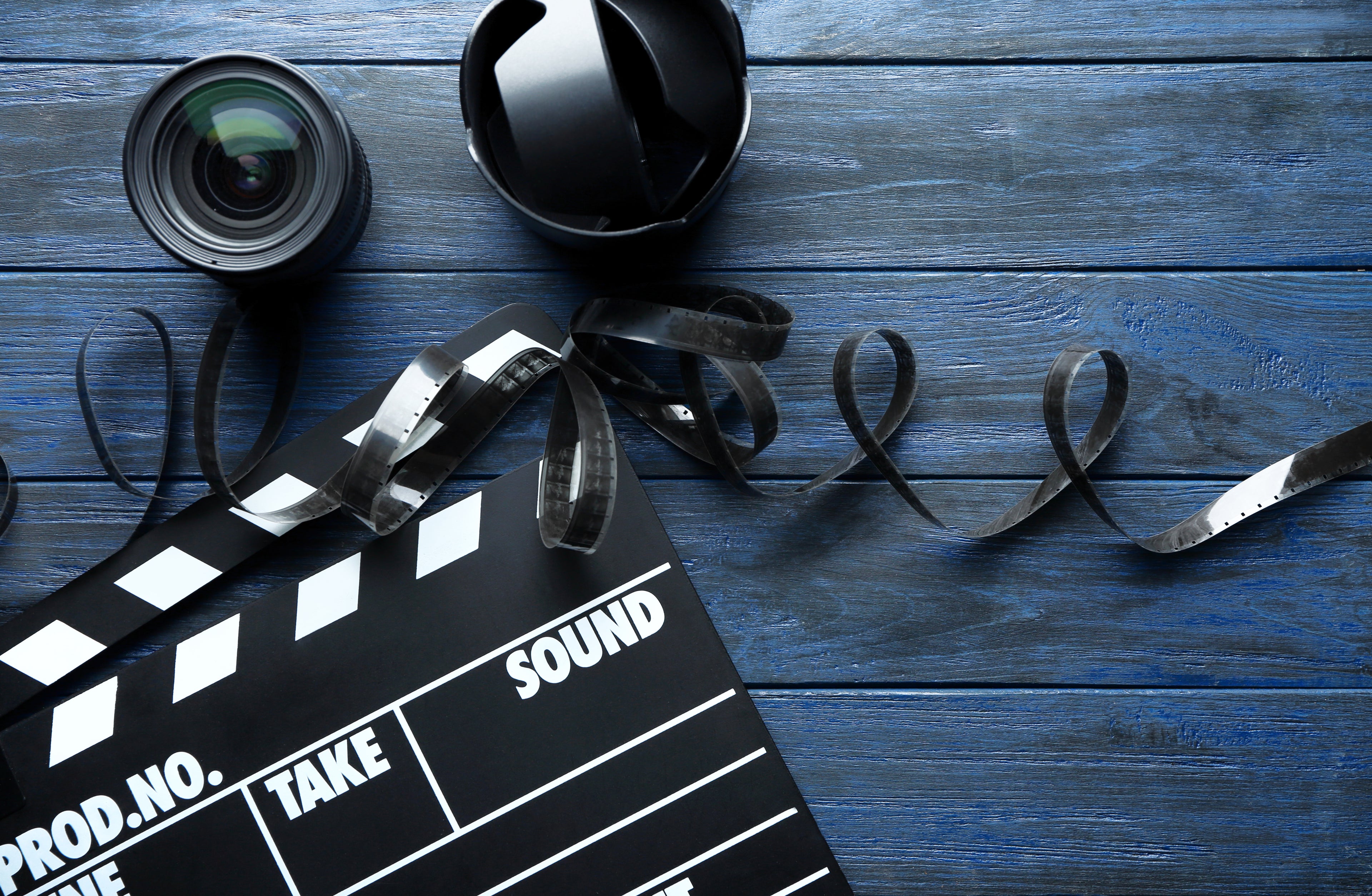 Clapperboard with movie camera and hat on a wooden surface