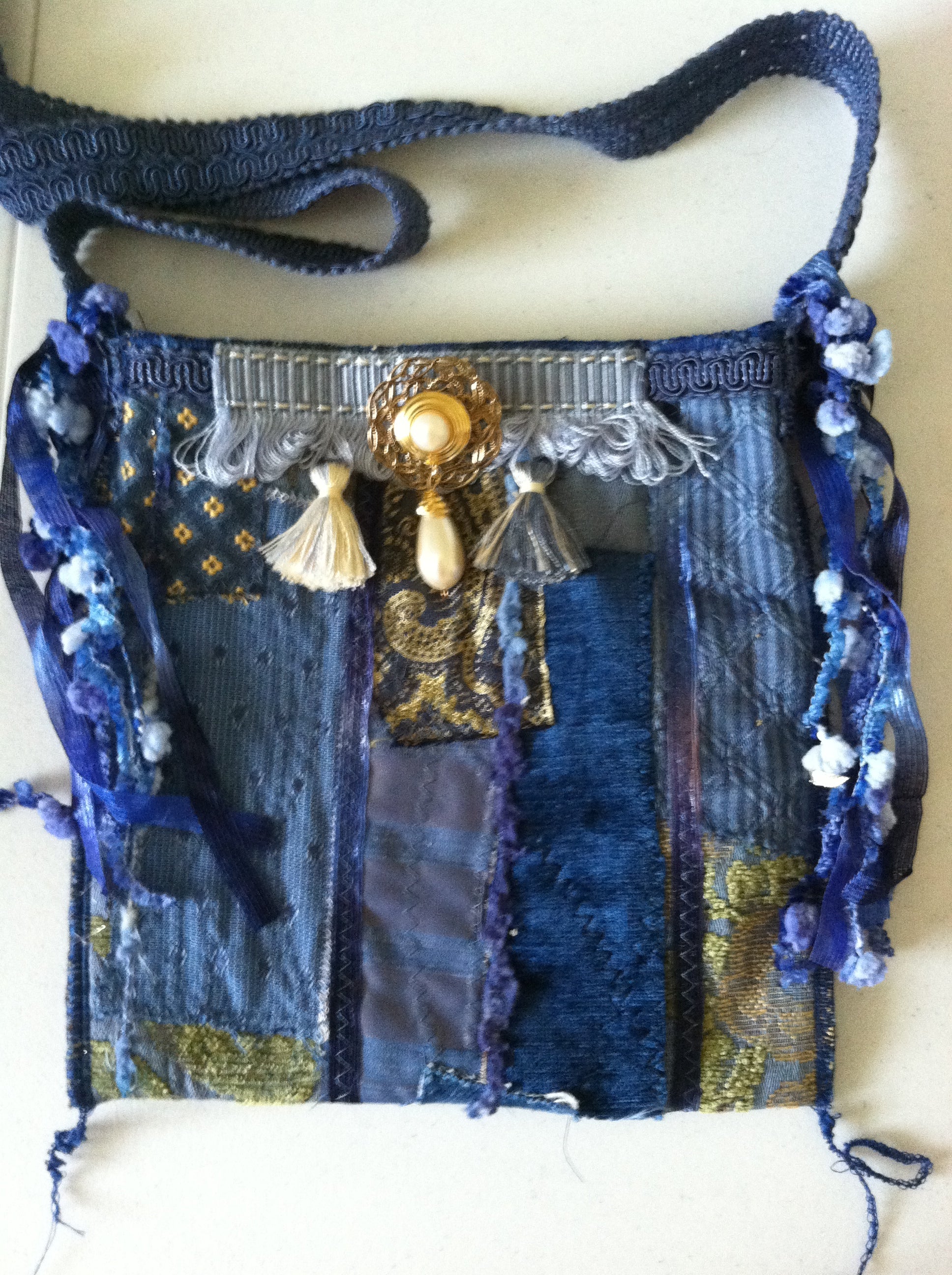 Decorative blue fabric handbag with intricate designs and embellishments on a white background